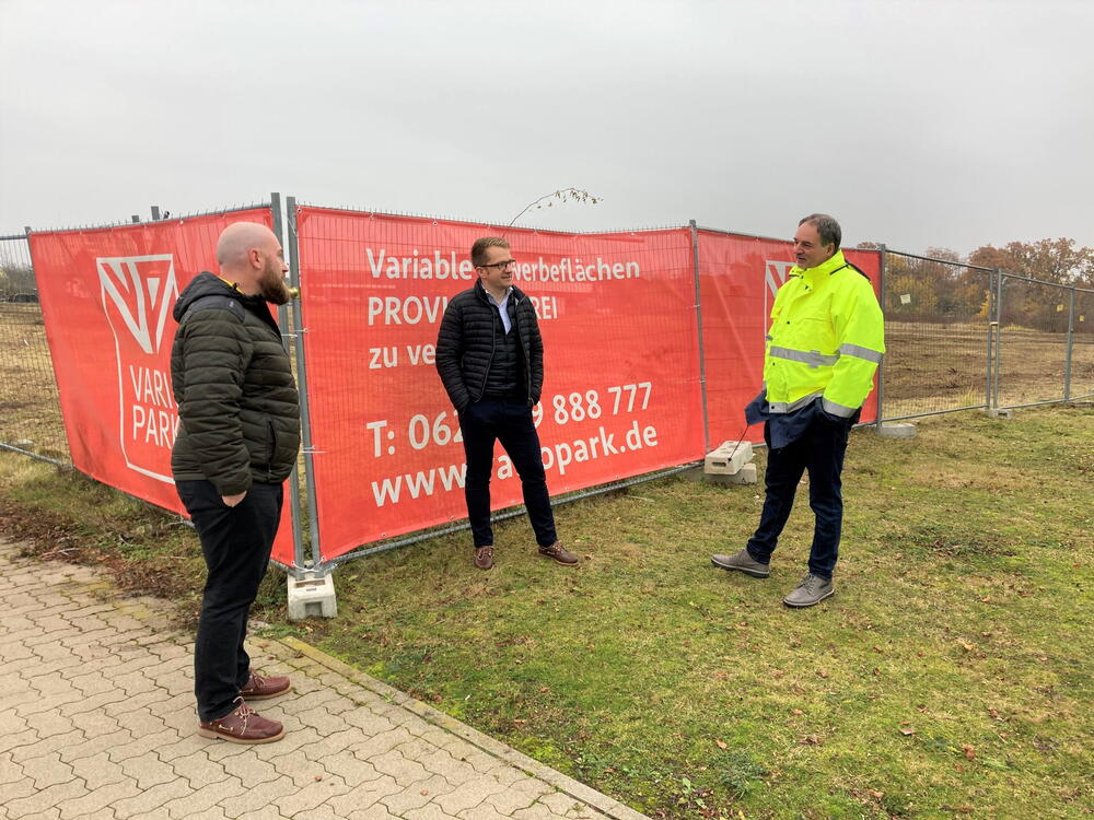Drei Projektbeteiligte vor Banner-Werbung am Baufeld in Frankenthal