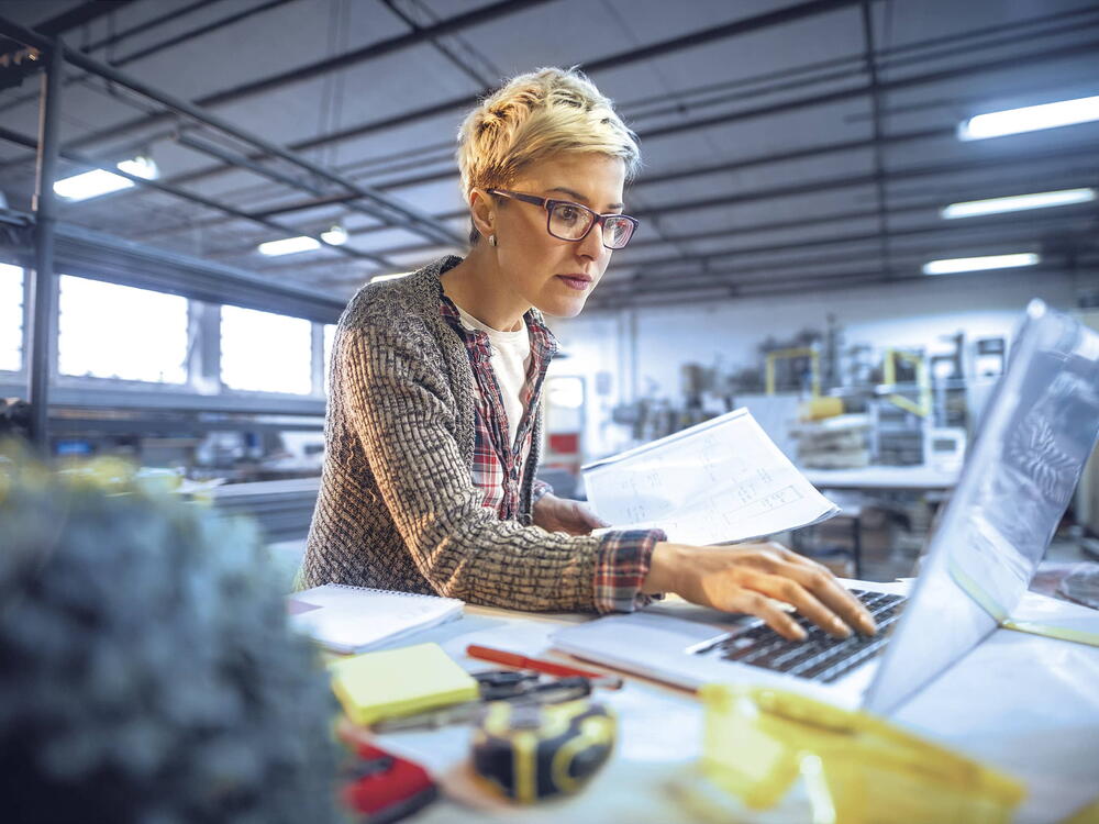 Foto einer VarioPark-Mieterin bei der Arbeit am Laptop im Hintergund industrielle Nutzung der Halle sichtbar